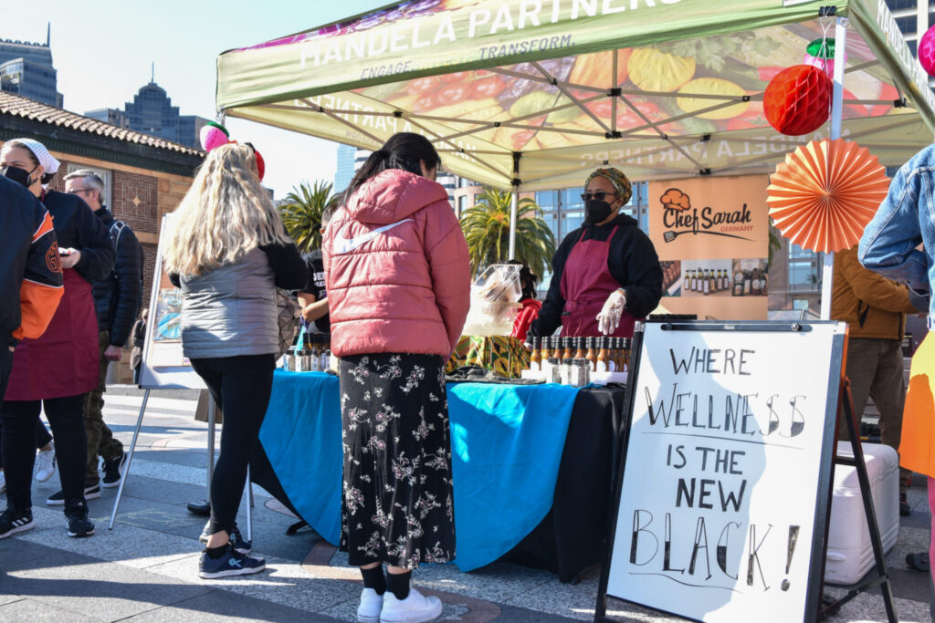 Chef Sarah Germany's booth on the plaza, with a sign that reads "Wellness is the new Black"