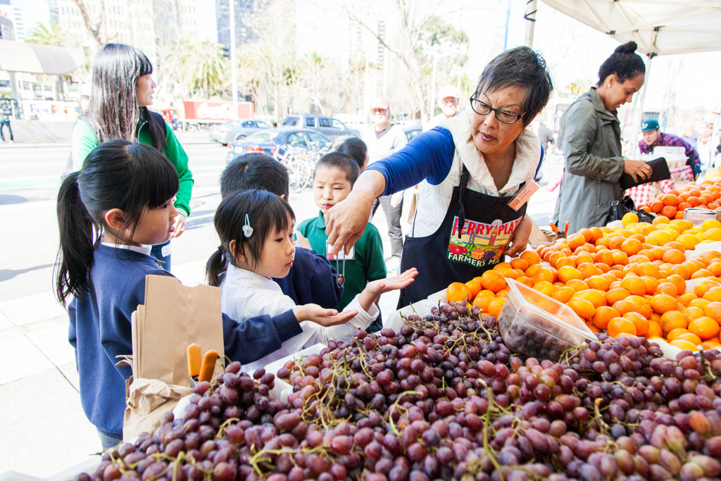 A Foodwise volunteer serving fruit to children at the Ferry Plaza Farmers Market