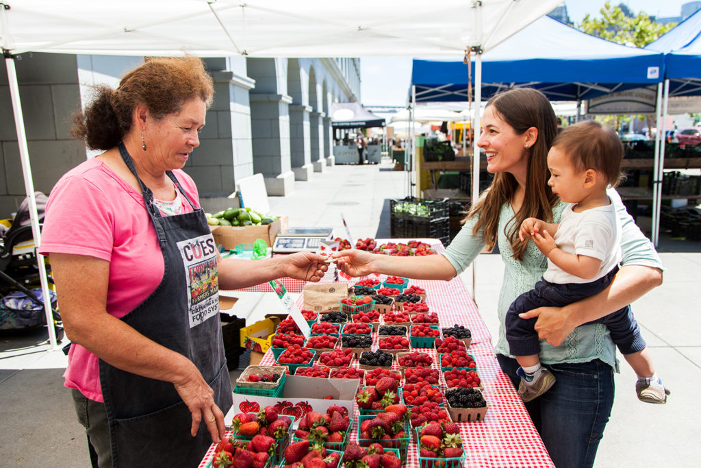 Young woman with a child using CalFresh EBT tokens to purchase produce at the Ferry Plaza Farmers Market