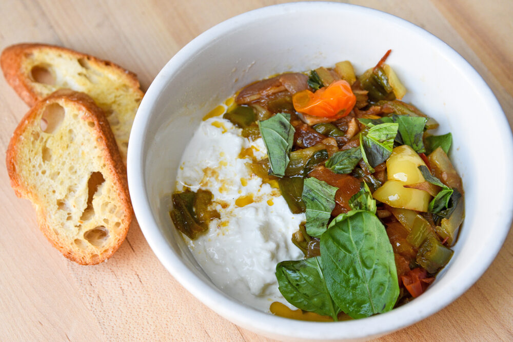 Bowl of peperonata (cooked summer vegetables) and cheese, with bread on the side