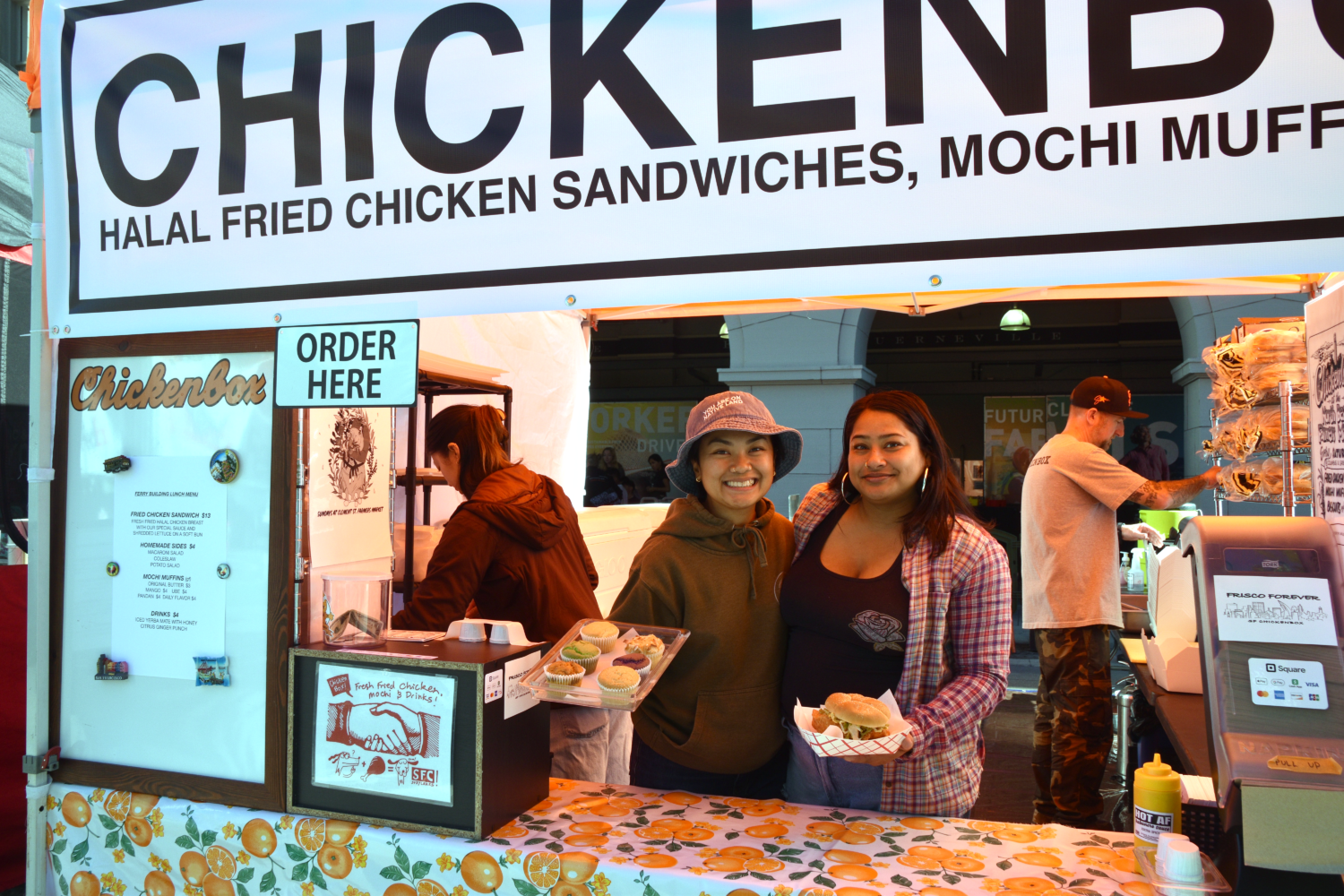 Two people, holding food, at the SF Chickenbox stand at the Ferry Plaza Farmers Market